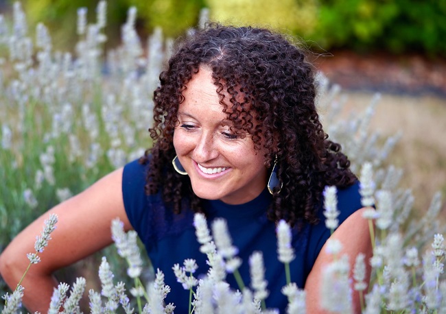 smiling woman sits amongst lavender plants